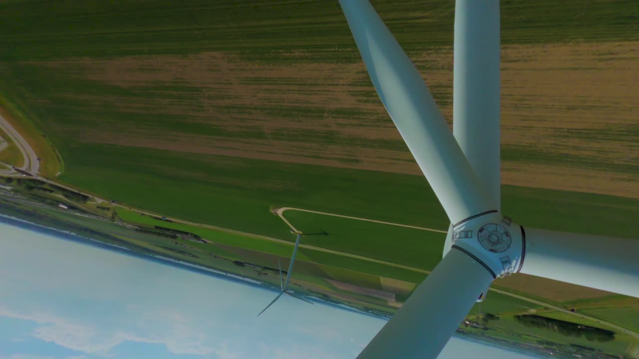 Aerial drone flight close to spinning blades on modern wind turbine in green field