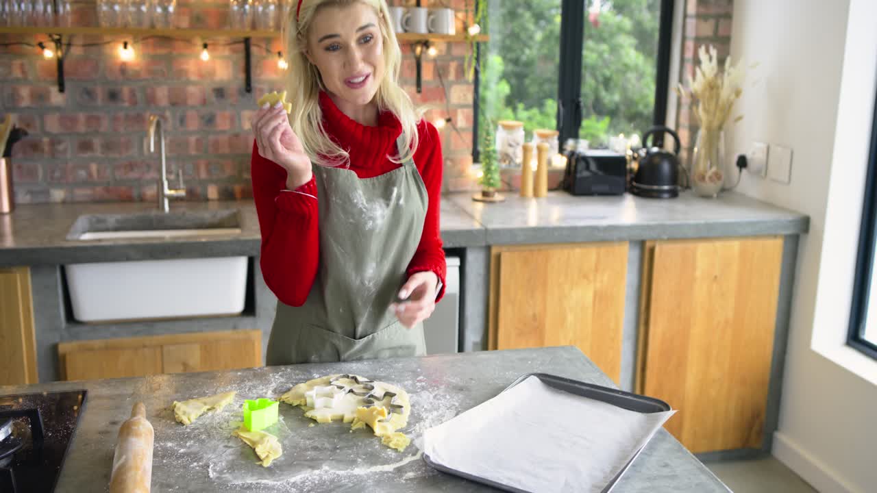 Female baker dusting flour on island, cutting shapes with cutter and placing cookies for baking