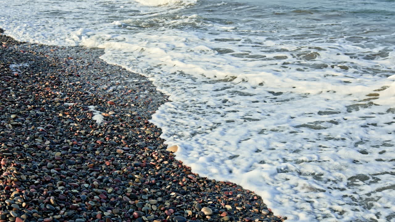 Sanfte Meereswellen spülen an einen bunten Kiesstrand.