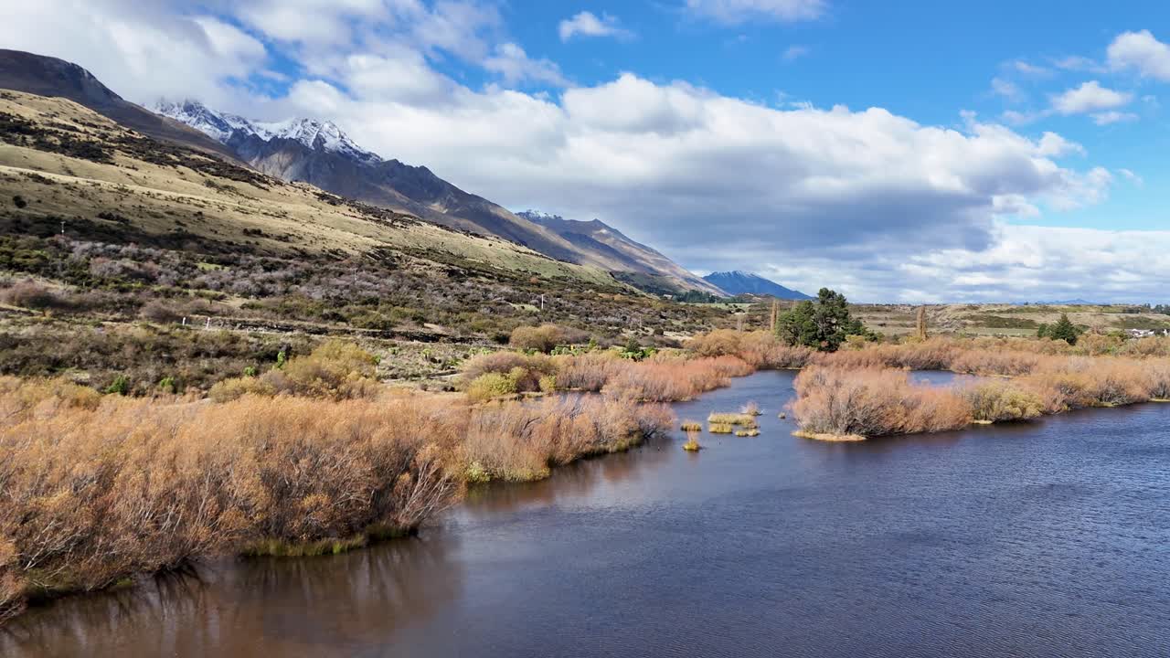 A tranquil river flows through Glenorchy's lush landscape under a bright sky, captured in vibrant daylight with gentle camera movement
