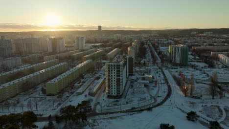he warm glow of the sunset bathes a snowy urban landscape, with residential buildings and roads etched into the winter scene, showcasing a blend of nature and city life in city gdańsk