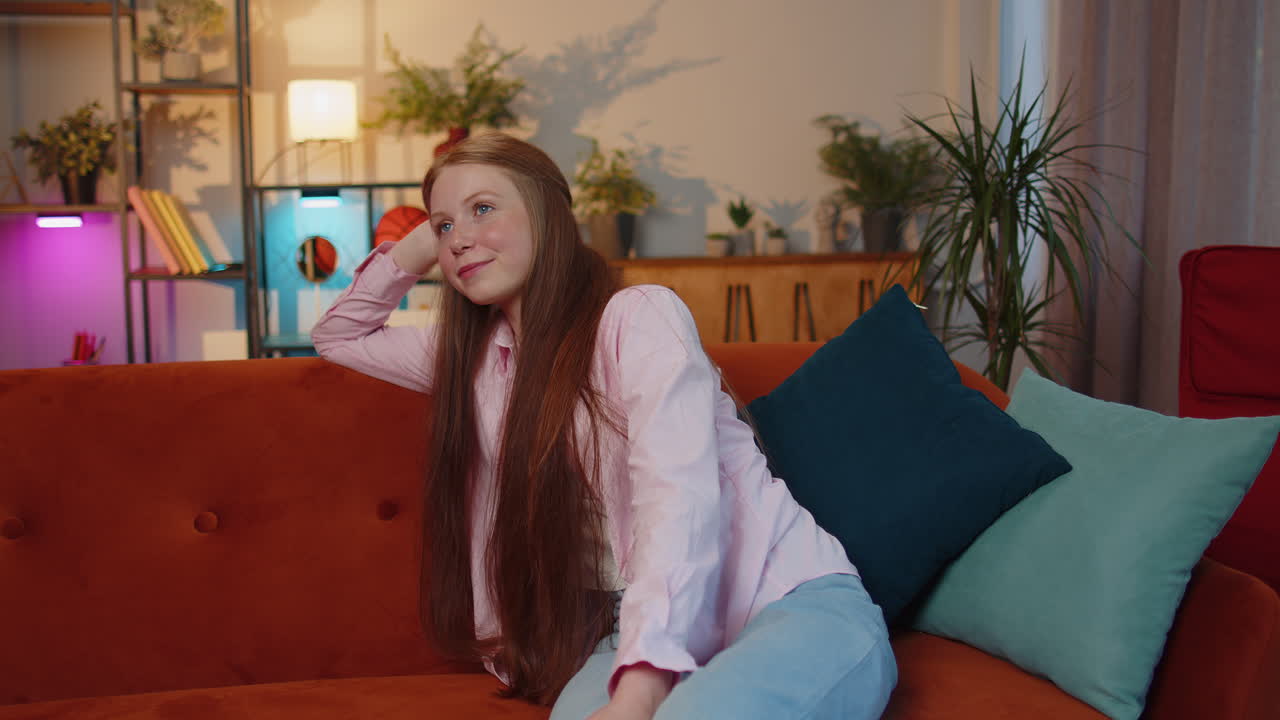 행복하고 평온한 젊은 여자가 미소 짓고, 멀리 바라보며, 꿈을 꾸고, 휴식을 취하고, 좋은 소식을 듣고, 집에서 사랑에 빠진다.