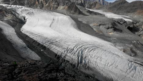 Aerial-flyover-over-a-hiker-overlooking-the-Allalin-and-Hohlaub-glacier-with-Allalinhorn-peak-in-view-near-Saas-Fee-in-Valais,-Switzerland-with-a-pan-down-view-down-the-cliff-to-the-ice-and-crevasses