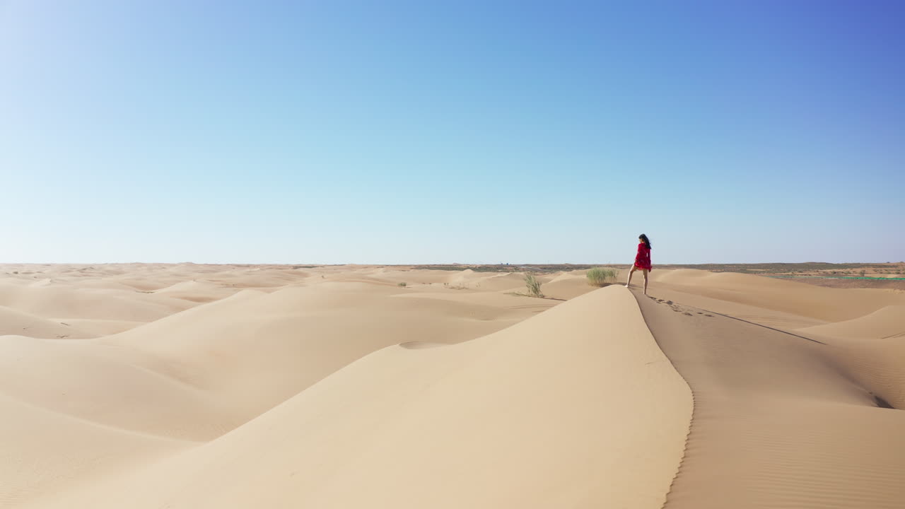 una fotografía de un dron cinematográfico de una mujer con un vestido rojo de pie en una duna de arena en el desierto de gobi