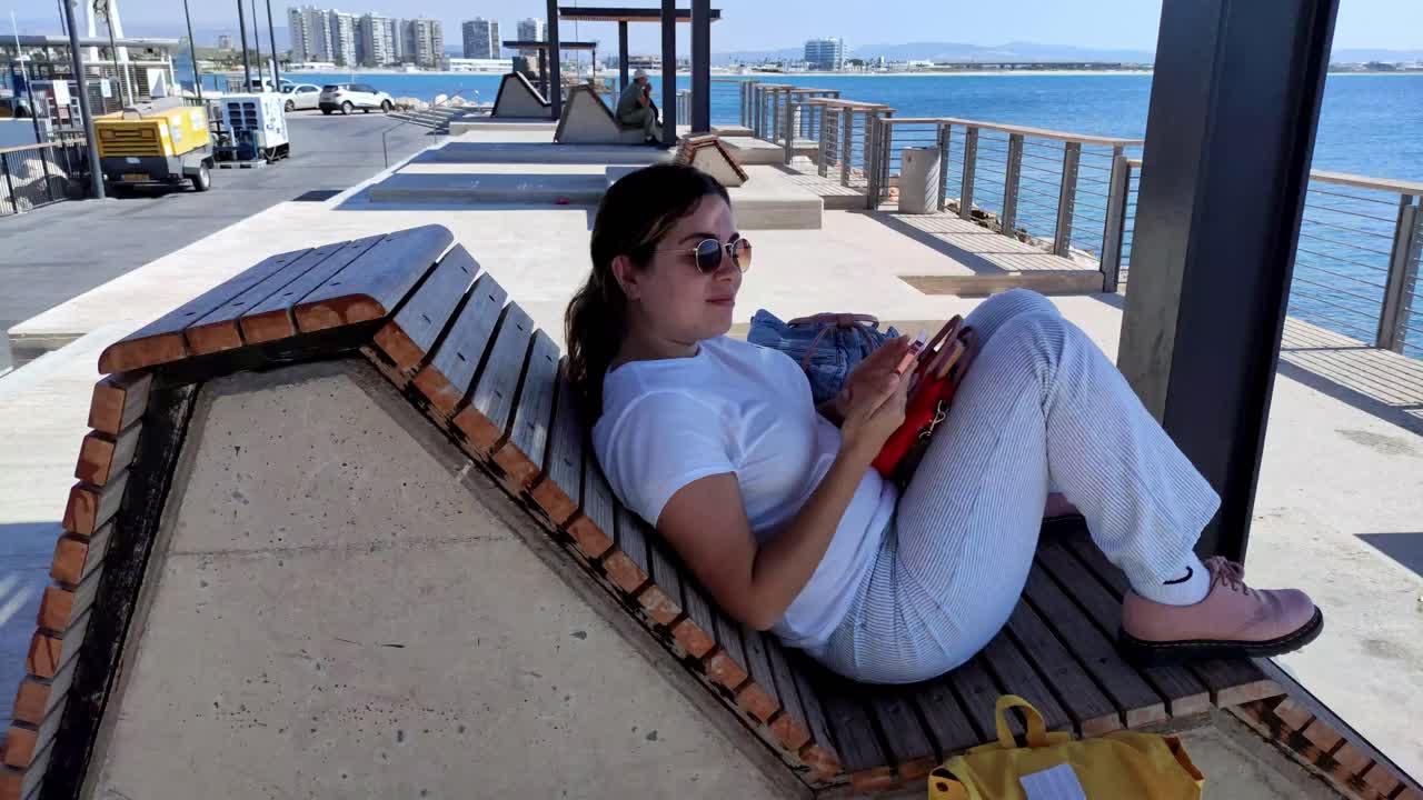 Happy young woman laughing while sitting on a seaside bench