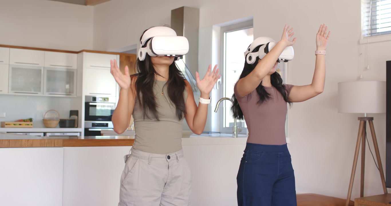 Amiche di diverse etnie in piedi in cucina, una sessione VR inizia, toccano visori bianchi e gesticolano.