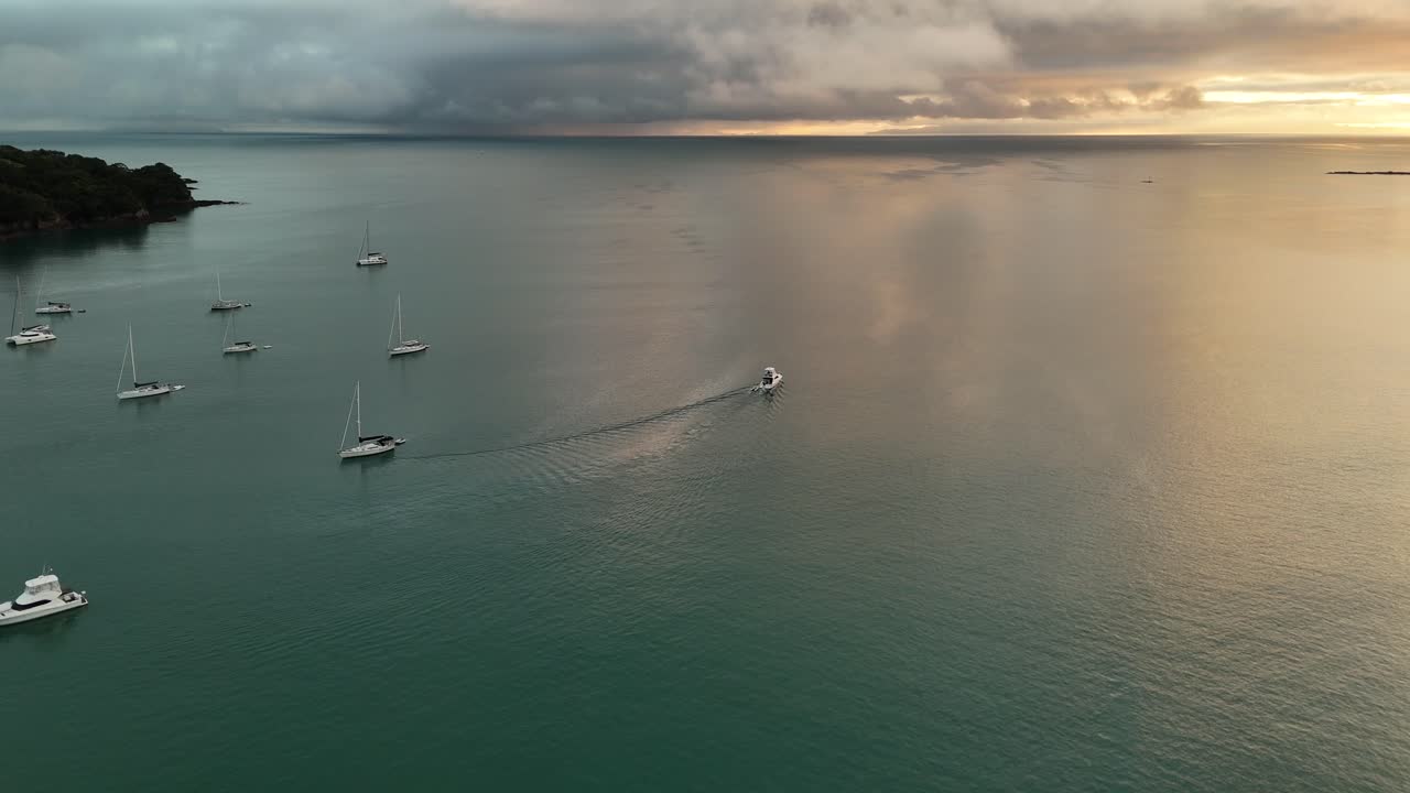 Sailing boats on water at Waiheke Island, New Zealand. Aerial wide shot. Golden sunsets in the evening. Tranquil sea bay in NZ. Clouds at sky.