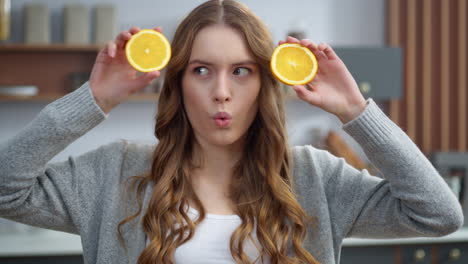 Emotional-girl-making-faces-with-oranges-at-kitchen.-Woman-changing-emotions