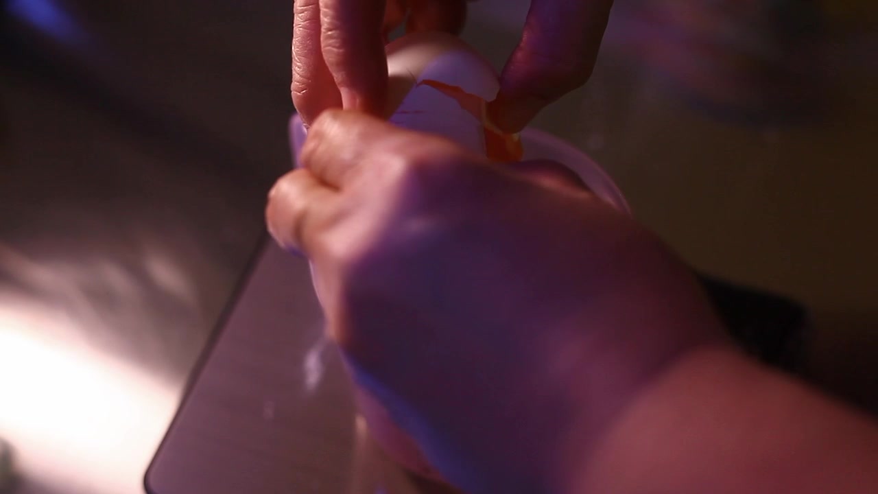 pair of hands cracking an egg to a measuring cup.