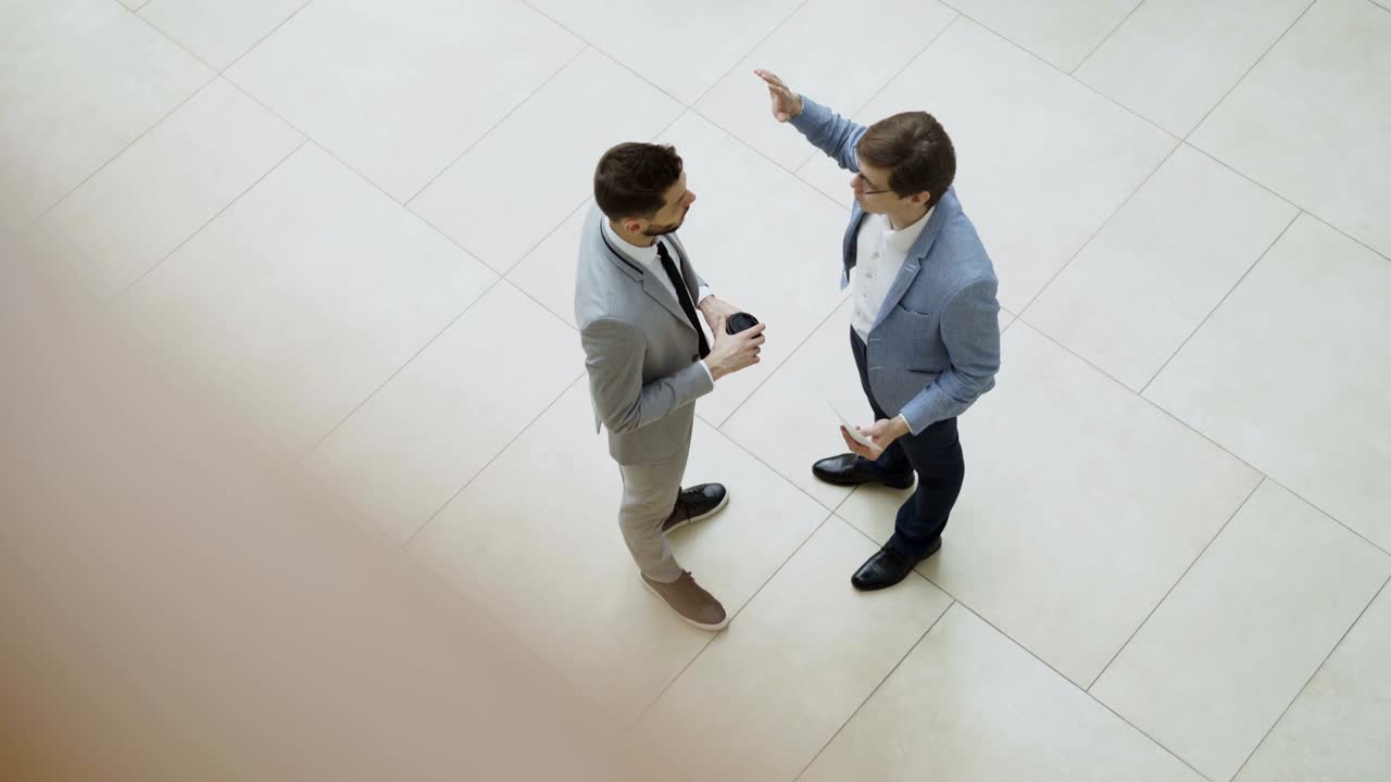 Vista dall'alto di due uomini d'affari che chiacchierano e discutono un rapporto finanziario nella hall di un centro direzionale.