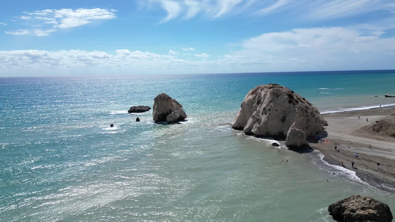 Drone tracking right orbit Petra tou Romiou beach with iconic sea rocks and turquoise Mediterranean water.