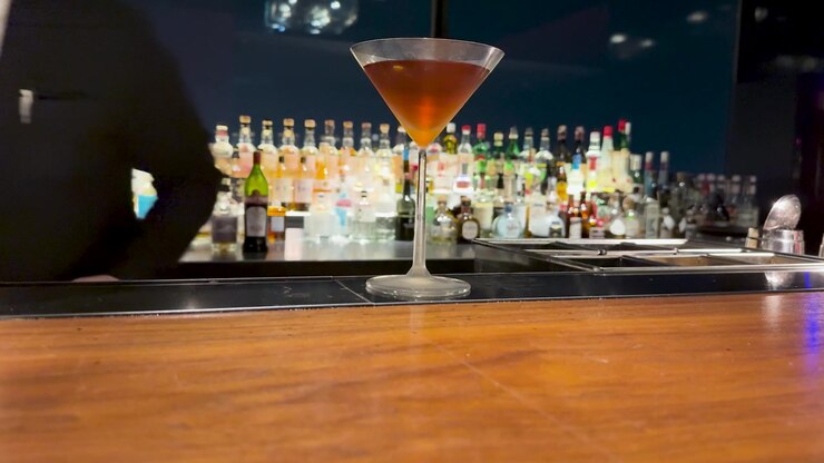 Un barman in abito nero prepara un martini al bancone di un bar in legno