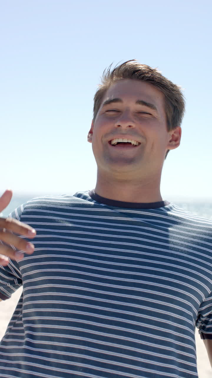 Vertical video: Smiling man enjoying sunny day at beach, wearing striped shirt