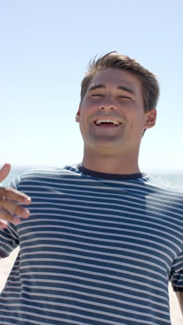 vertical video: smiling man enjoying sunny day at beach, wearing striped shirt