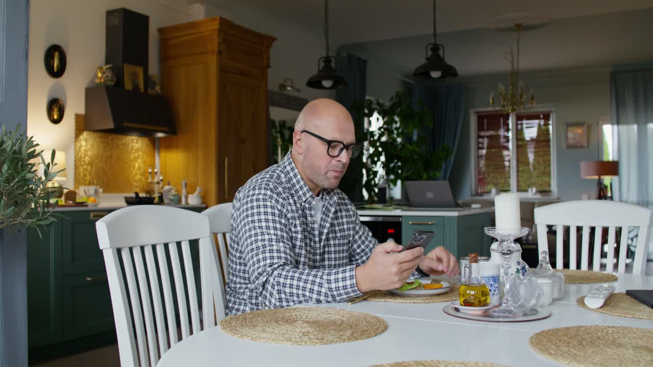 Man Eating and Using Phone at Dining Table