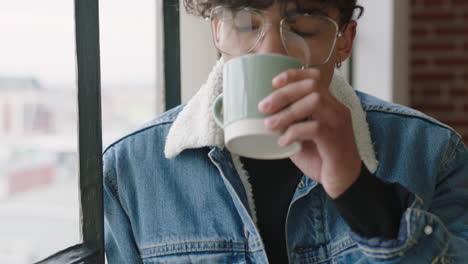 Elegante-Joven-Estudiante-Hispano-Tomando-Café-En-Casa-Mirando-Por-La-Ventana-Pensando-En-Planificar-Con-Anticipación-Disfrutando-De-Un-Estilo-De-Vida-Relajante-Usando-Gafas-De-Moda