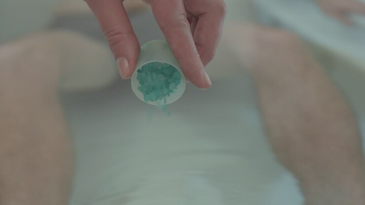 Close-up shot of crystals being poured into a spa bath with legs behind