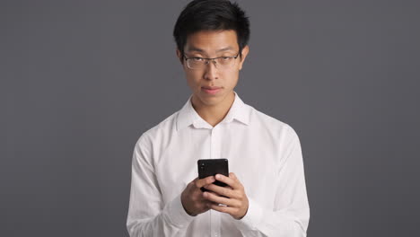 Asian-man-using-smartphone-and-smiling-to-the-camera.