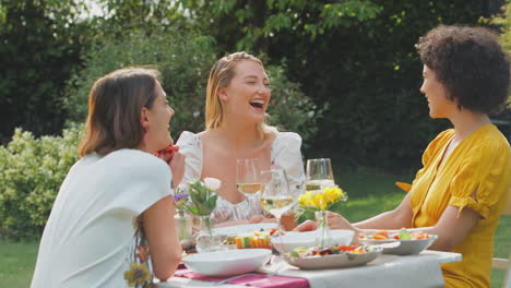 tres amigas sentadas al aire libre en el jardín de verano en casa bebiendo vino y comiendo comida