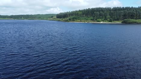 Idyllic-blue-water-reservoir-lake-woodland-hiking-walk-aerial-view-pull-back-through-trees-foliage
