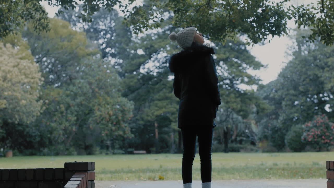 추운 겨울날 비니 모자를 쓰고 나무를 바라보며 자연을 즐기고 있는 정원 공원의 젊은 여성