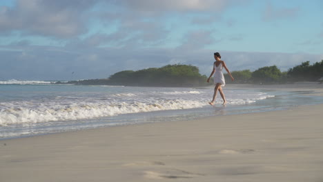 beautiful female traveller getting her feet wet by tortuga bay beach waves in the galapagos. slow motion