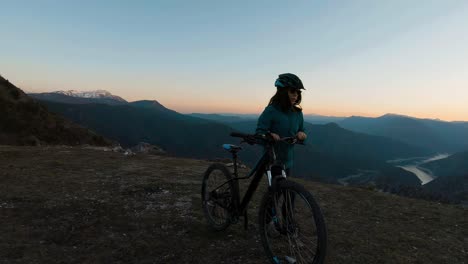 girl pushing her bike on a mountain hill at sunset with beautiful canyon lake in the background