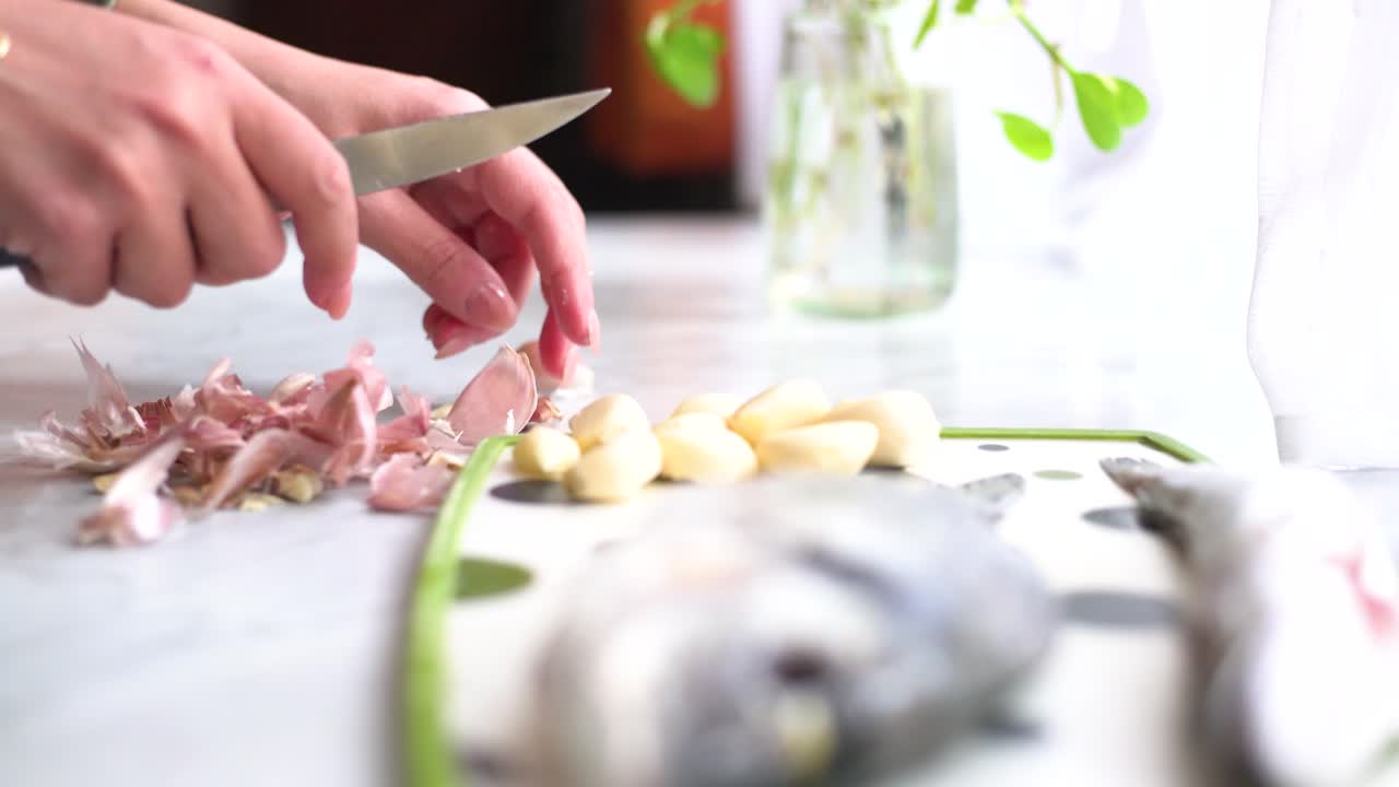hand peeling garlic next to a sea bream and a whiting on the work surface