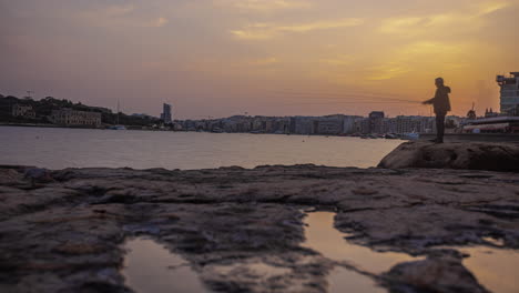 Hombre-Pescando-Al-Atardecer-A-Lo-Largo-De-La-Costa-Maltesa-Cerca-De-Sliema---Lapso-De-Tiempo-Dorado