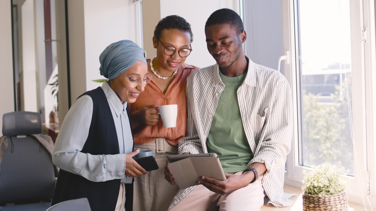 이슬람 사업가, 사업가, 젊은 노동자가 사무실에서 태블릿을 보면서 웃고 있다 1