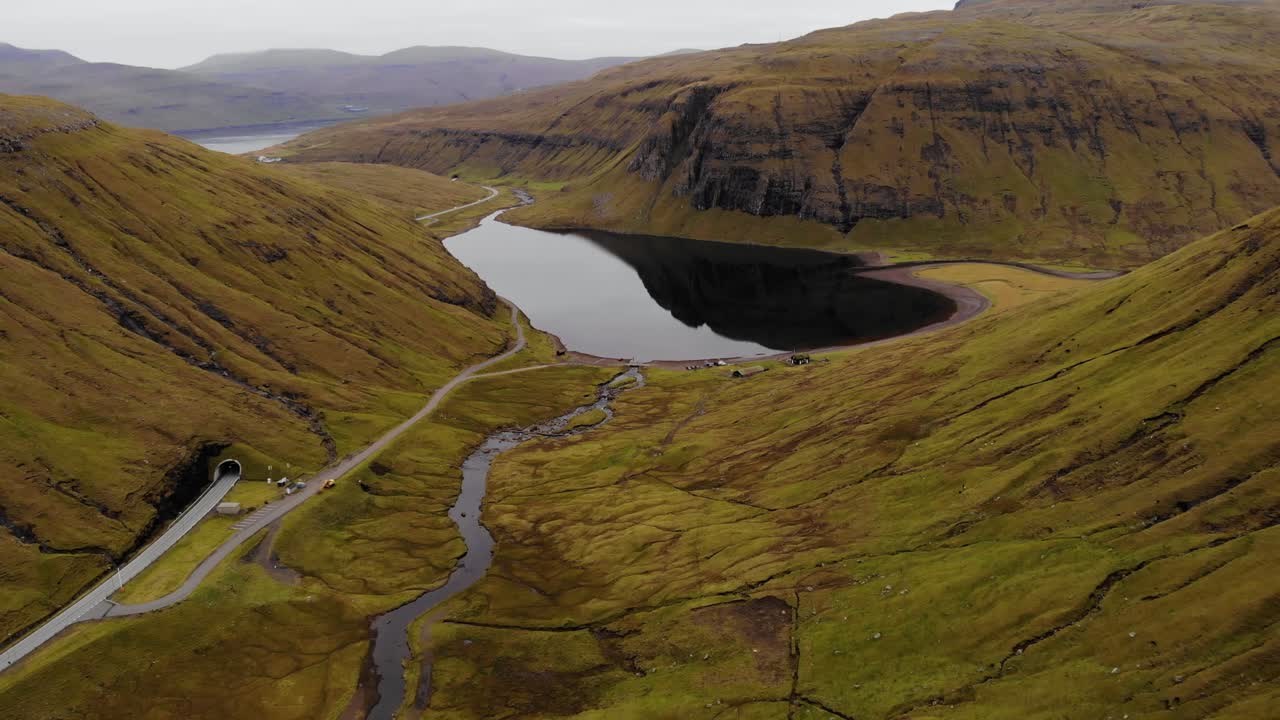 ángulo alto aéreo del hermoso lago y río reflectantes en las montañas verdes de las islas feroe con una carretera y un túnel al lado