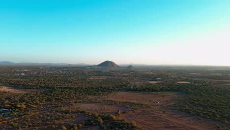 estableciendo el disparo del dron avanzando hacia el pico de la montaña rodeado de un rico cielo azul, vegetación verde y suelo marrón-naranja