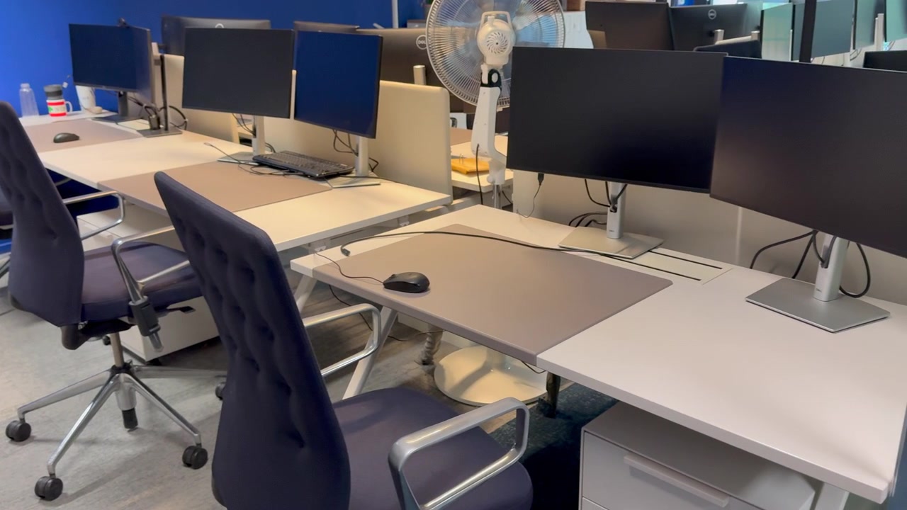 An empty modern office featuring multiple computer monitors ergonomic chairs and clean minimalist desks