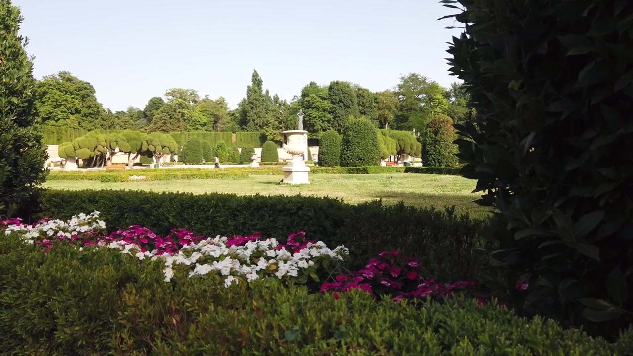 Langsame Schwenkfahrt des Parterre-Gartens im Retiro-Park, Madrid, Spanien, mit Blumenbeeten, Landschaft und Formschnittbäumen.