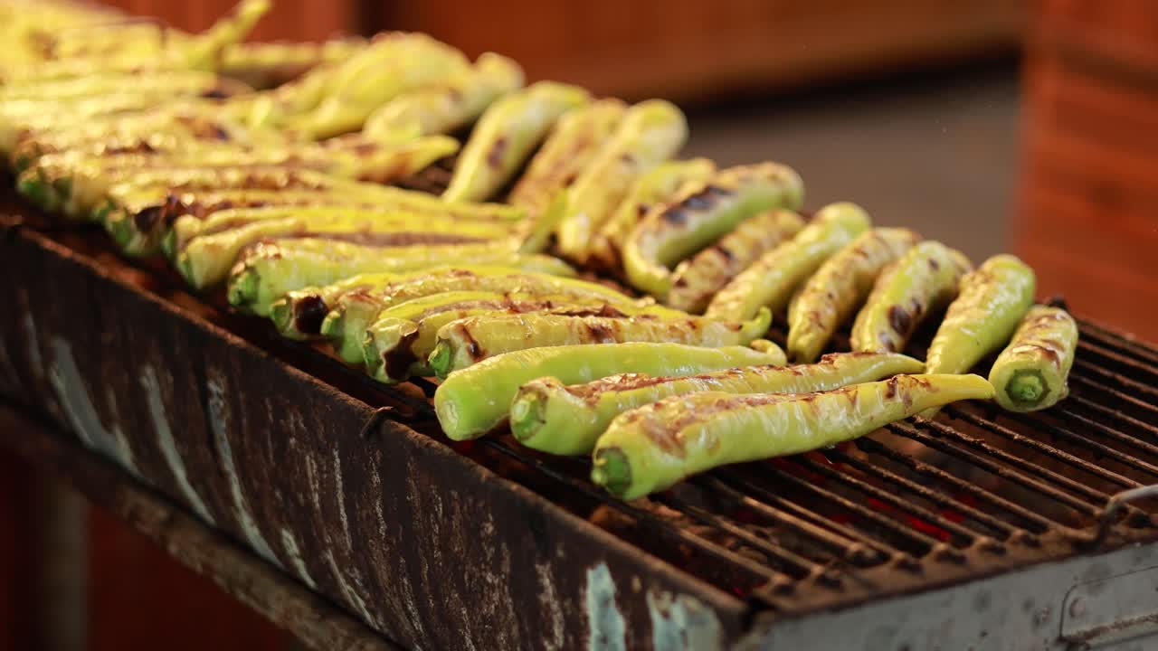 Chilies grilling on a rustic barbecue at a vibrant market. Warm lighting enhances the fresh, appetizing scene
