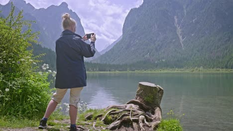 woman tourists takes phone photo of scenic lake with mountain backdrop