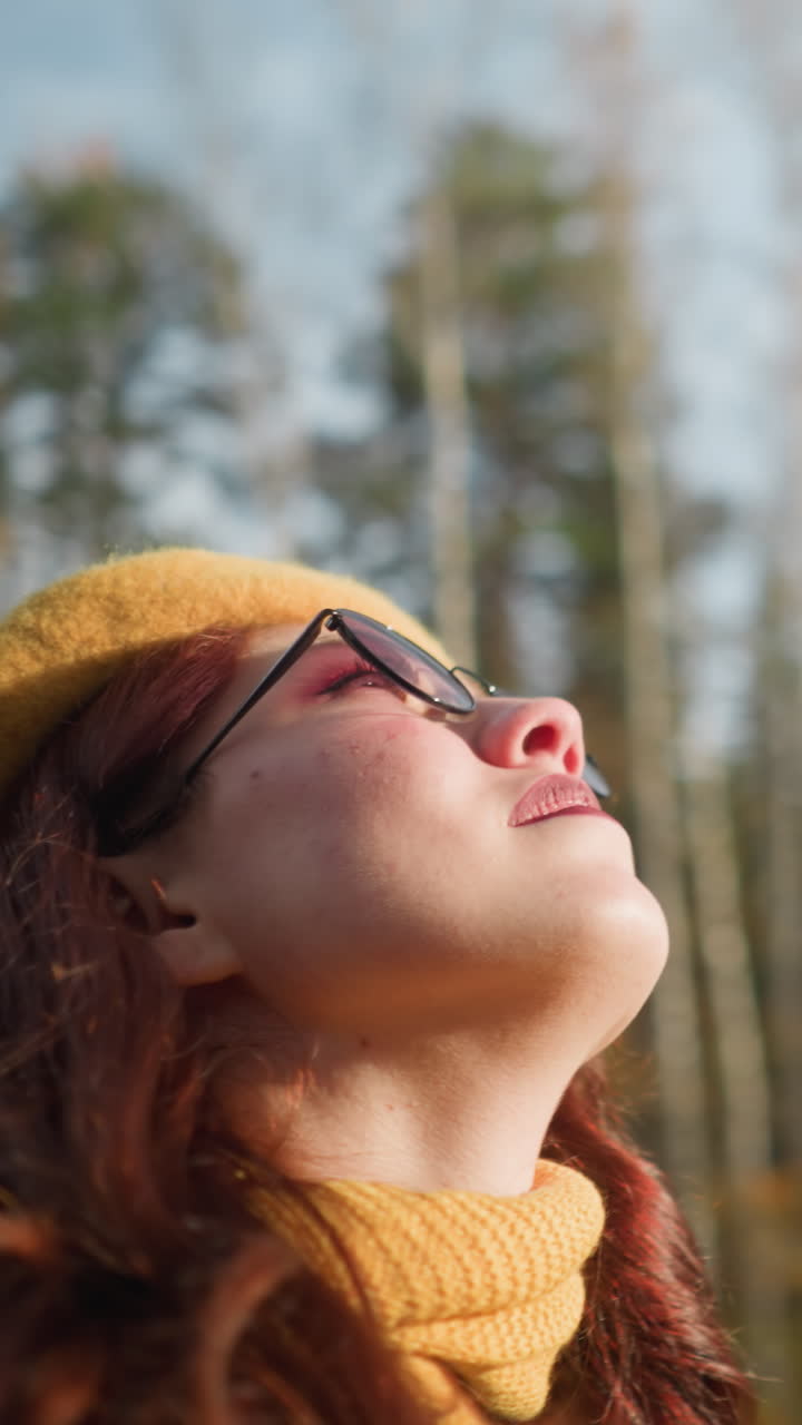 dama elegante con boina amarilla y gafas de sol disfruta de la naturaleza vista panorámica con árboles en el fondo, la luz del sol crea un brillo suave mientras mira hacia arriba, apreciando la belleza del otoño