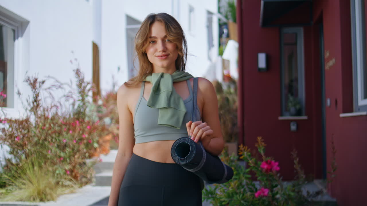 Woman holding yoga mat outdoors in sunny residential area. Carefree lady posing