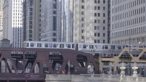 grey subway train rides over rusty steel bridge in chicago downtown skyline