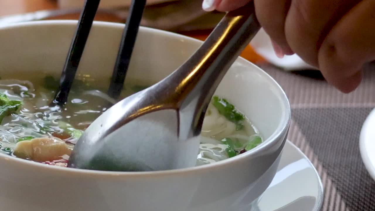 A detailed view of noodle soup being enjoyed with chopsticks and a spoon, highlighting fresh ingredients.