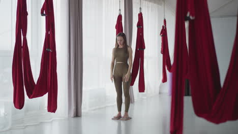 female athlete practicing quietness barefoot on nail boards in spa like studio surrounded by red hammocks meditating balancing mind body sensory focus under serene ambient peaceful concentration