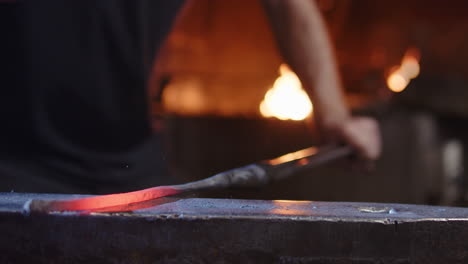 Blacksmith hammering a red hot iron on an anvil, forge fire burns in background