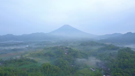 Luftaufnahme-Der-Ländlichen-Landschaft-Am-Nebligen-Morgen-Mit-Riesigen-Bergen-Im-Hintergrund