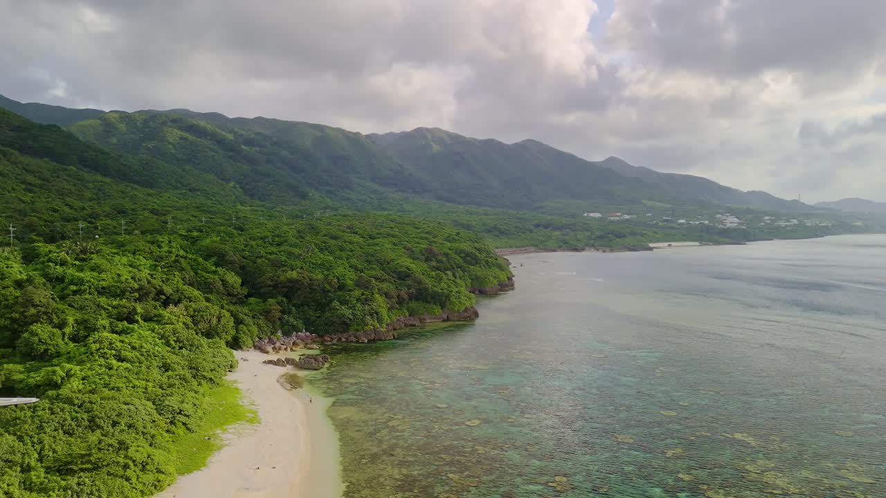 Ripresa cinematografica con drone che scivola su barriere coralline e sabbie bianche verso le fitte foreste tropicali e le spettacolari creste montuose dell'isola di Ishigaki all'ora d'oro