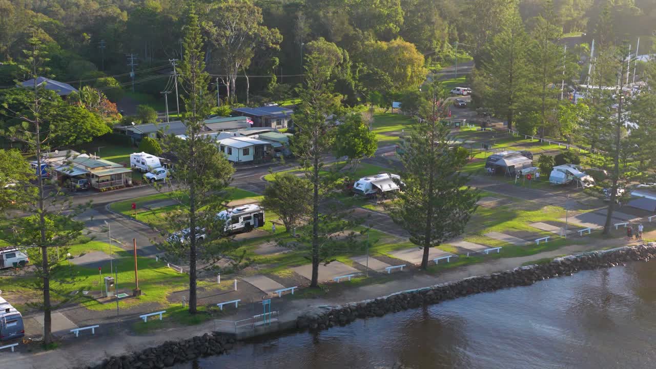 Aerial footage of a serene riverside campground in Brunswick Heads, NSW, showcasing lush greenery and parked caravans under soft, natural lighting