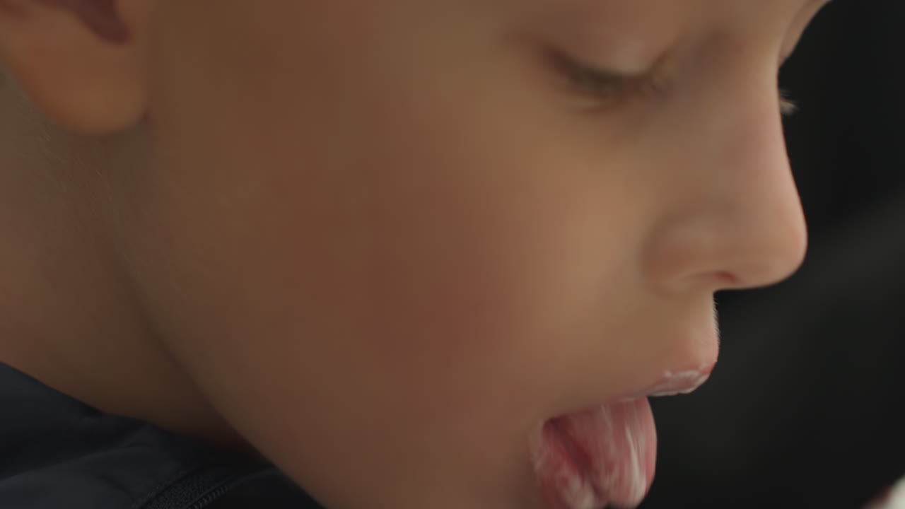 Primo piano di un ragazzo che assaggia un cono waffle, lenta attenzione sensoriale su lingua e labbra mentre il gelato cremoso si scioglie contro la consistenza croccante del waffle, scatto di profilo spontaneo, luce naturale, atmosfera intima da ASMR alimentare, giovanile.