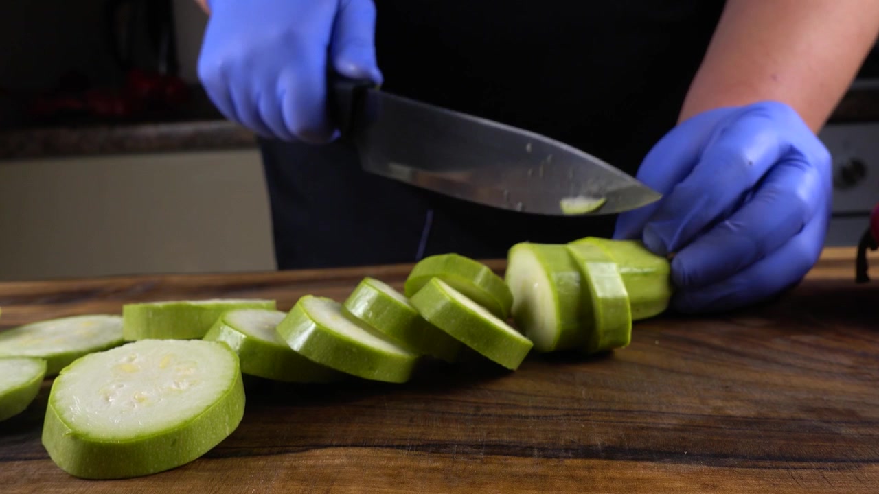 The cook cuts vegetable marrow on a cutting board.