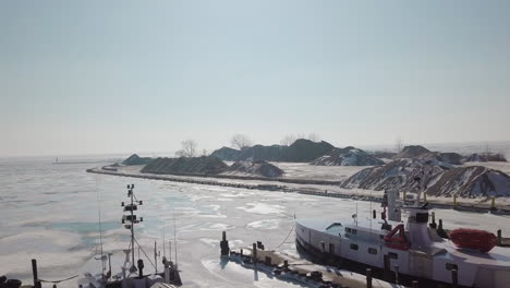 Drone-shot-of-boats-in-a-frozen-harbour-and-stone-quarry-along-lake-erie-in-Ontario,-Canada-in-the-middle-of-winter