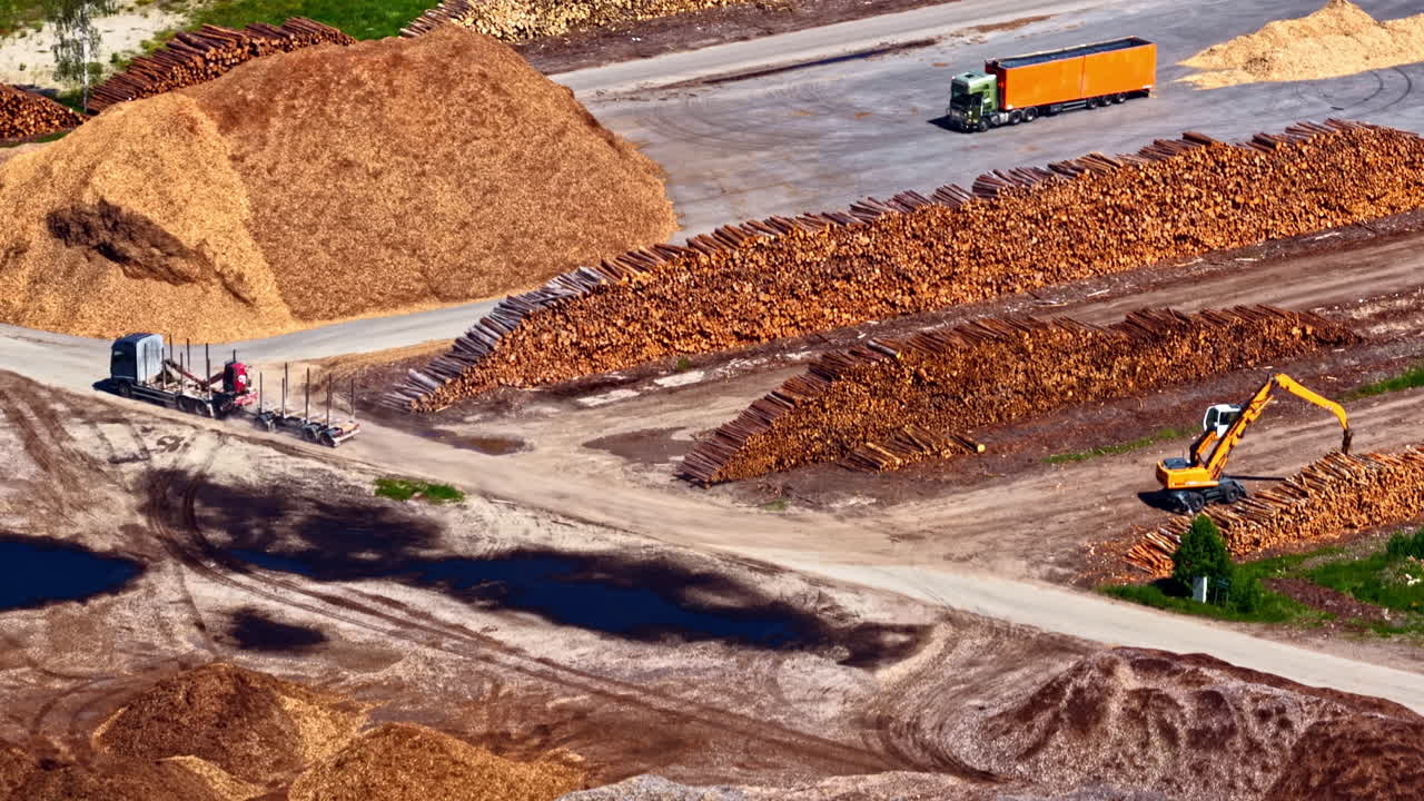 Aerial view of wood processing facility with large piles of logs, woodchips and sawdust