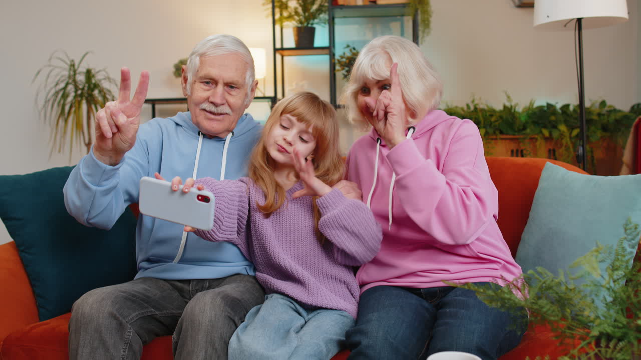 Child girl granddaughter with grandparents make blogger selfie smartphone portrait shows peace sign